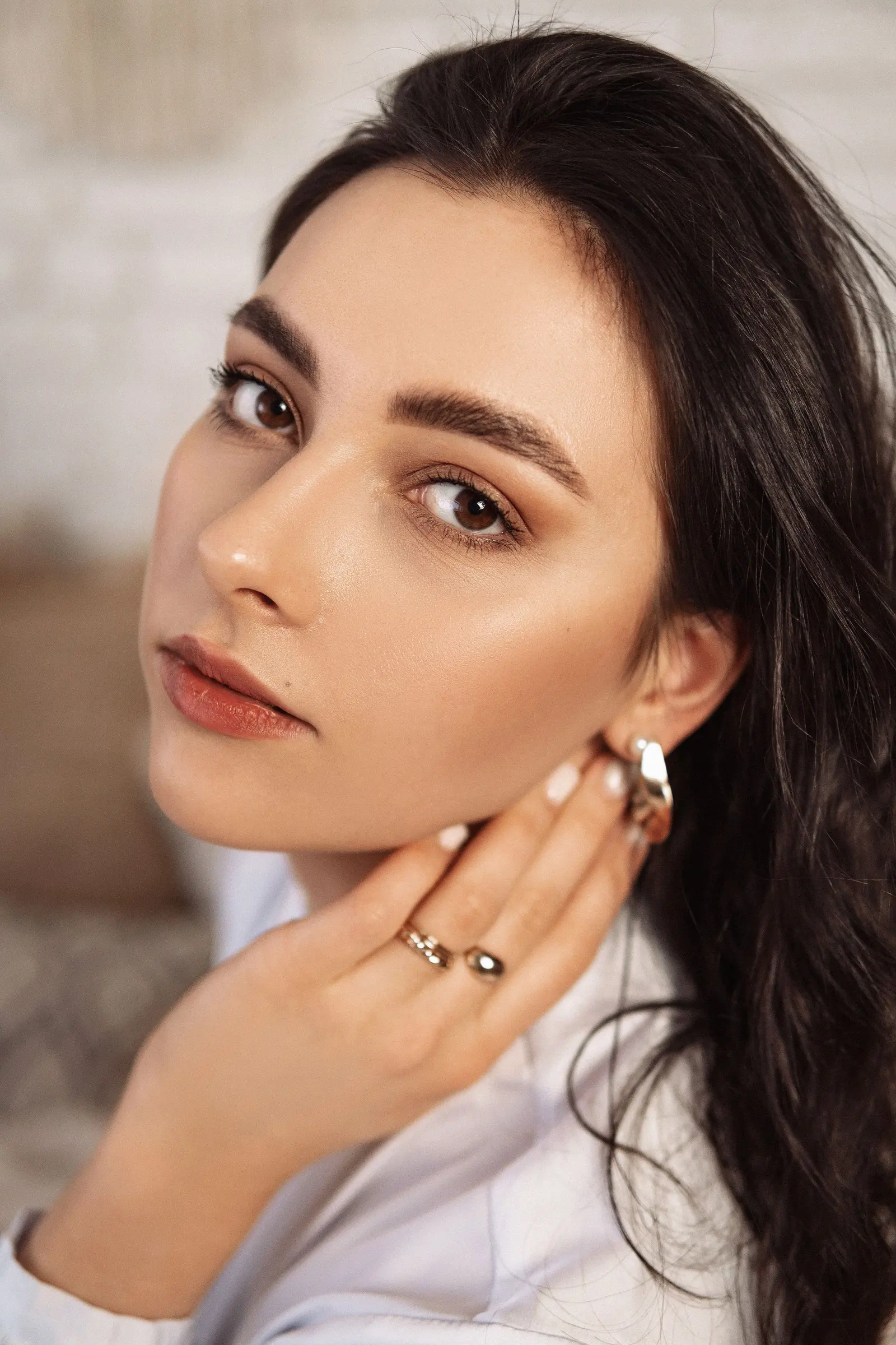 Woman with natural, glowing skin touching her neck in warm light
